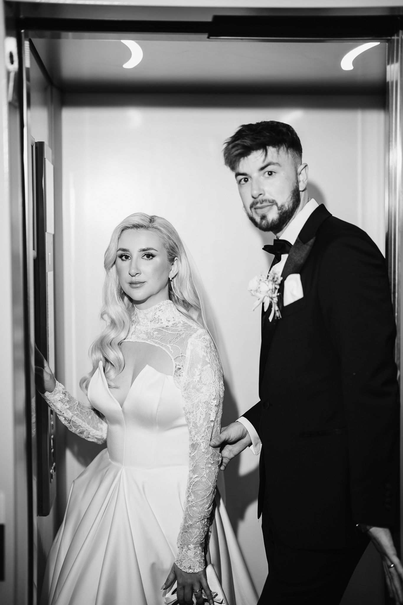 Couple in wedding attire pose in elevator during their special day.
