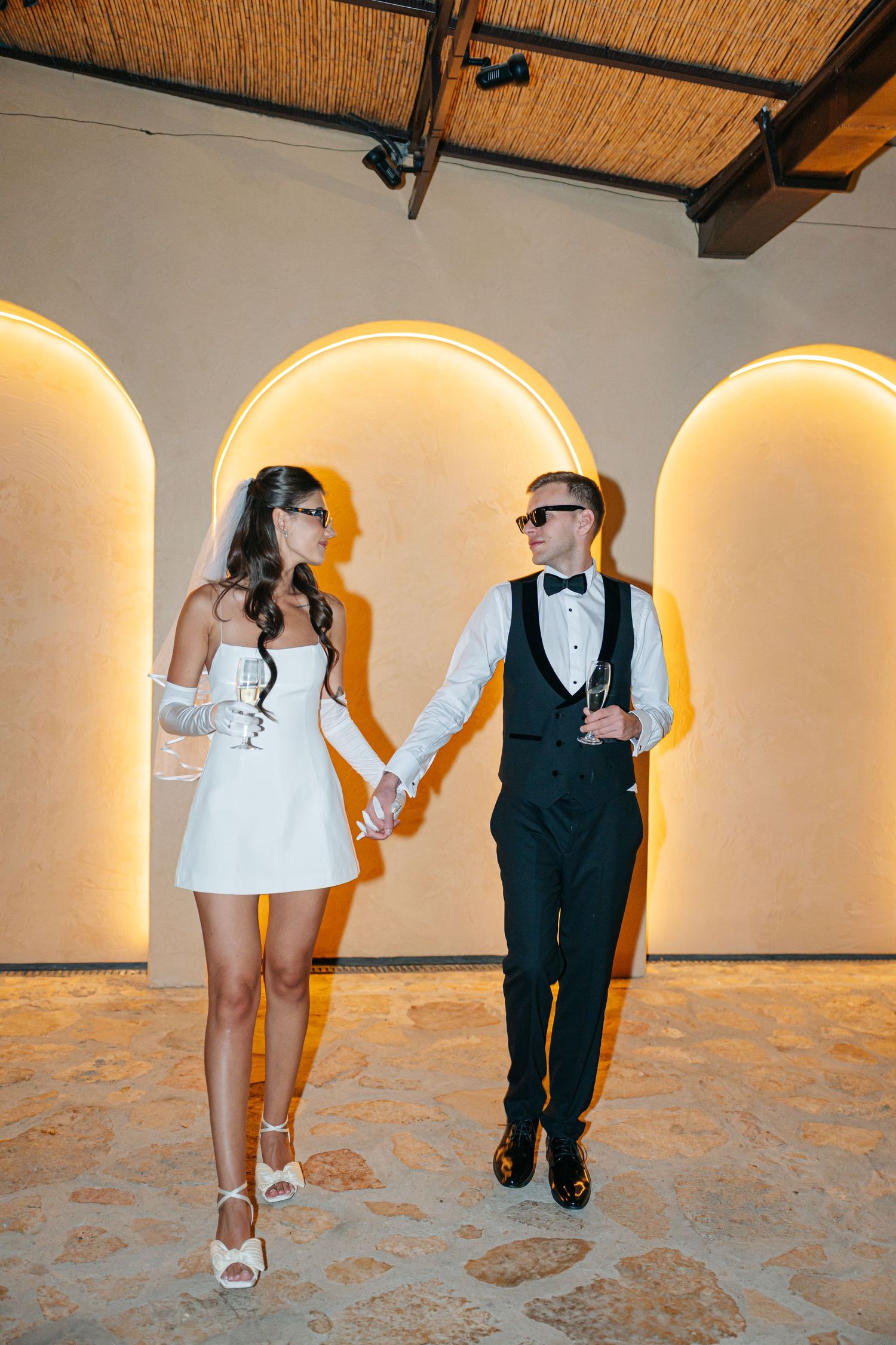 A series of artistic wedding photos showing feet and formal attire against a rustic wall with arched alcoves.