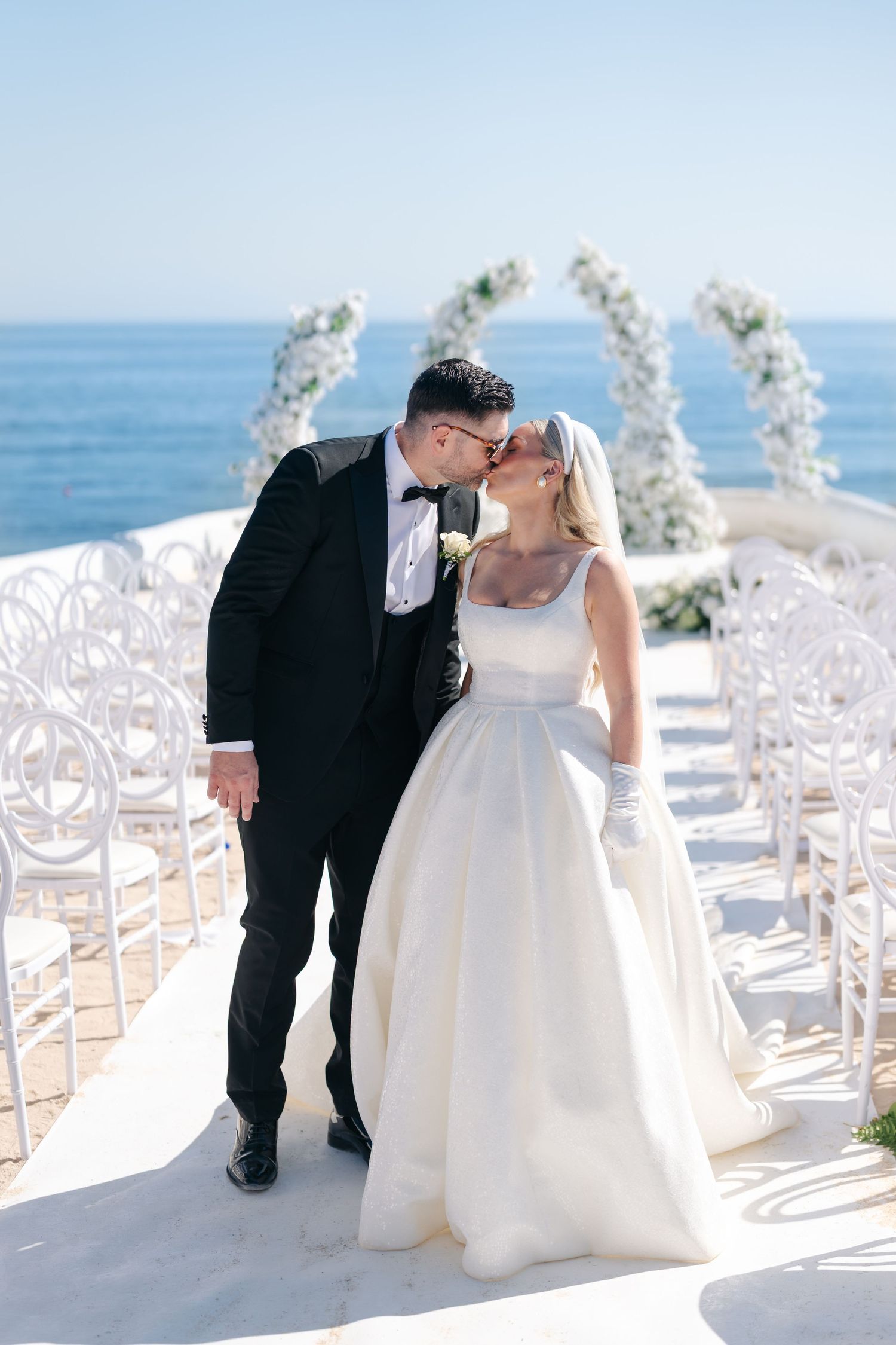 Wedding couple shares intimate moments on a terrace with white chairs and floral decor.