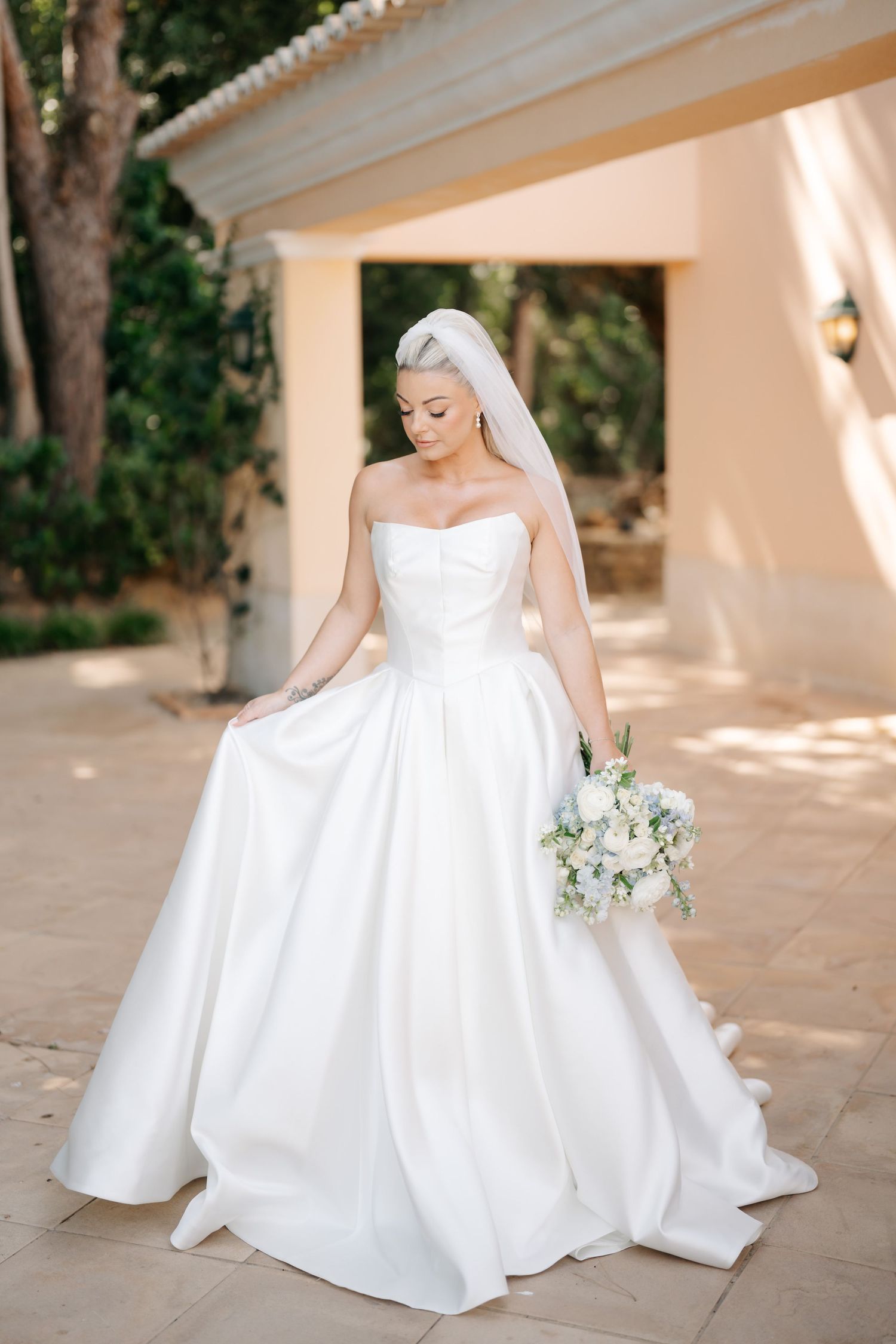 Elegant bridal portraits featuring a classic white ballgown in a sun-dappled courtyard.