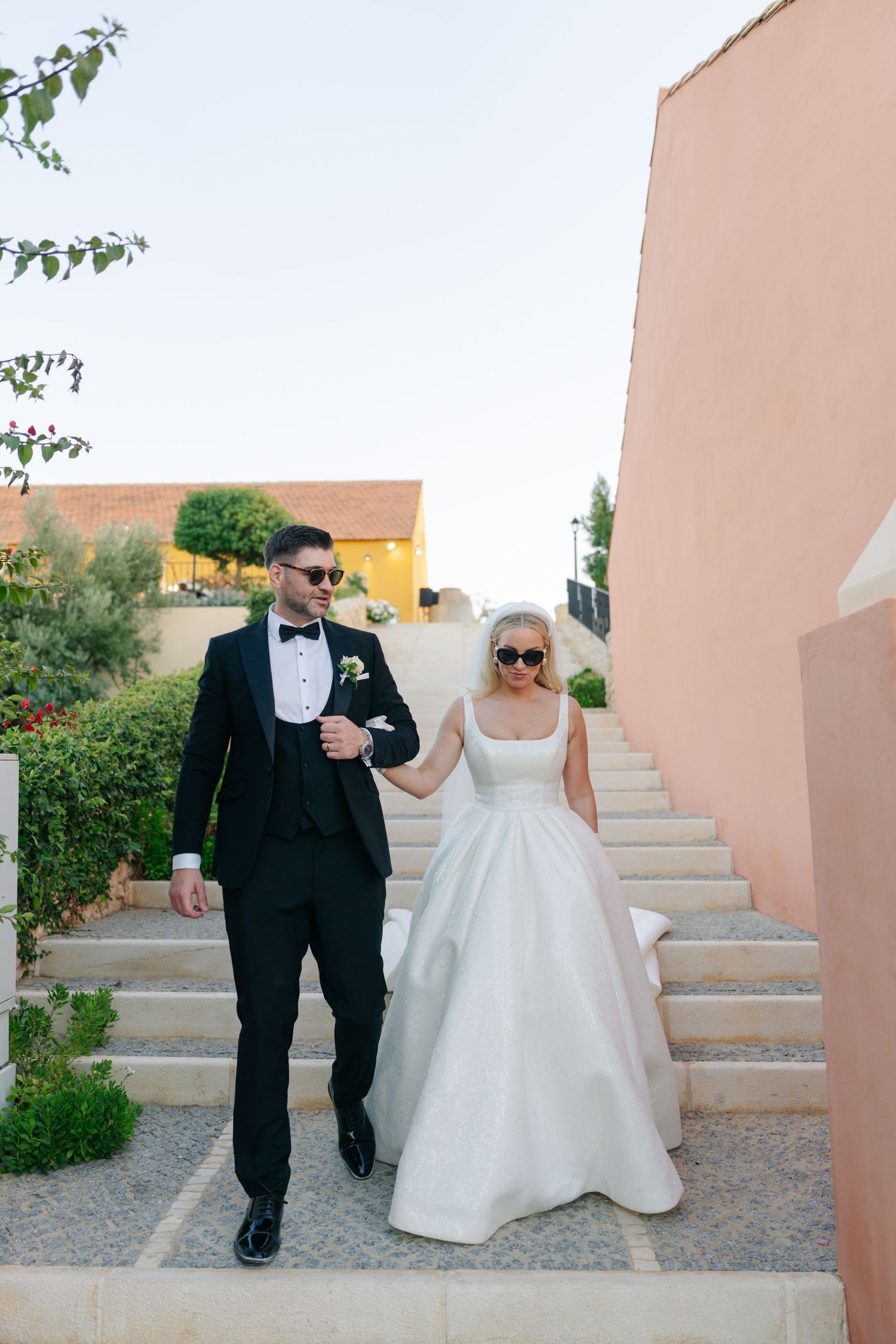 Wedding couple descends pink stucco stairs together at a Mediterranean-style venue.