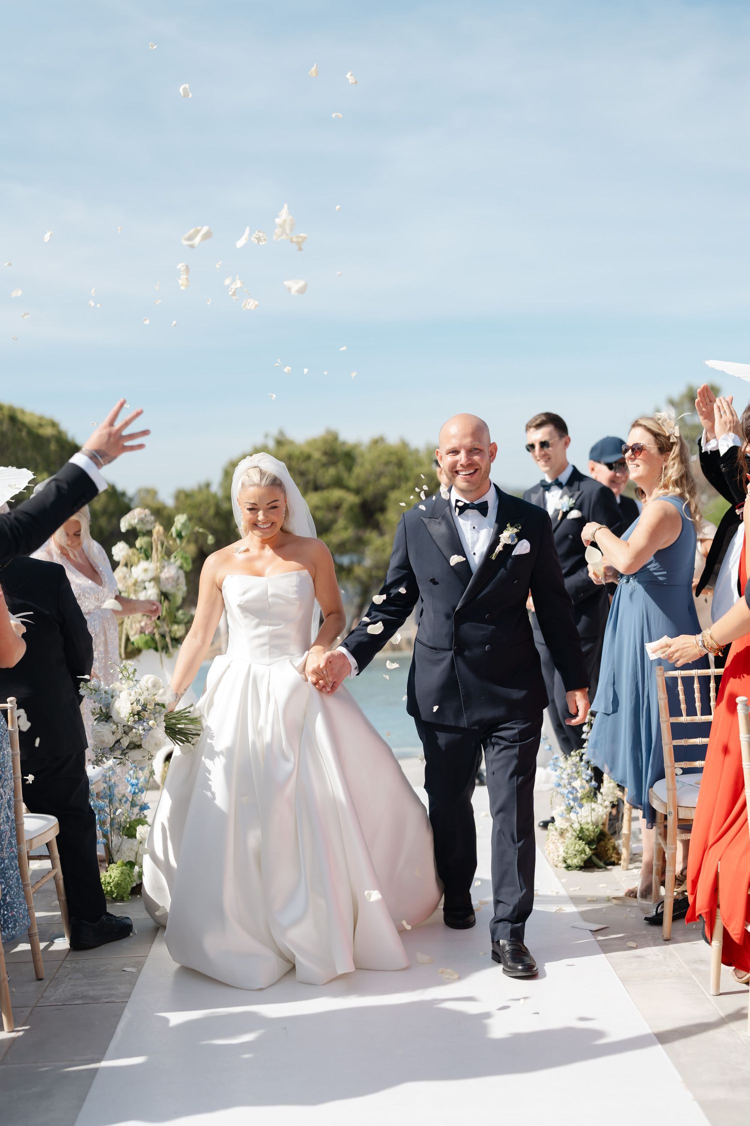 Wedding celebration with guests throwing confetti during outdoor waterfront ceremony.