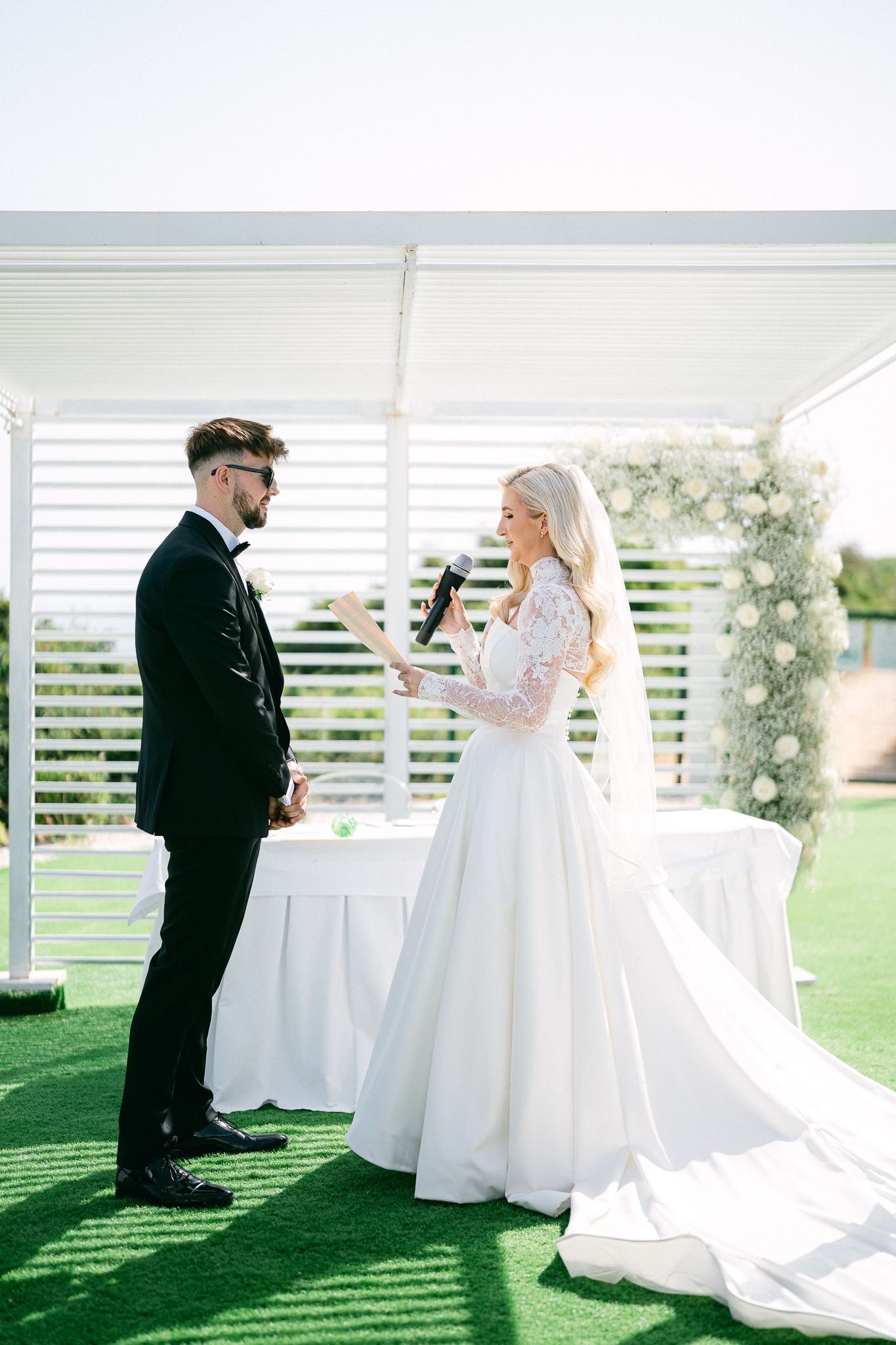 Intimate first look moment between newlyweds under a white pergola on a grassy lawn.