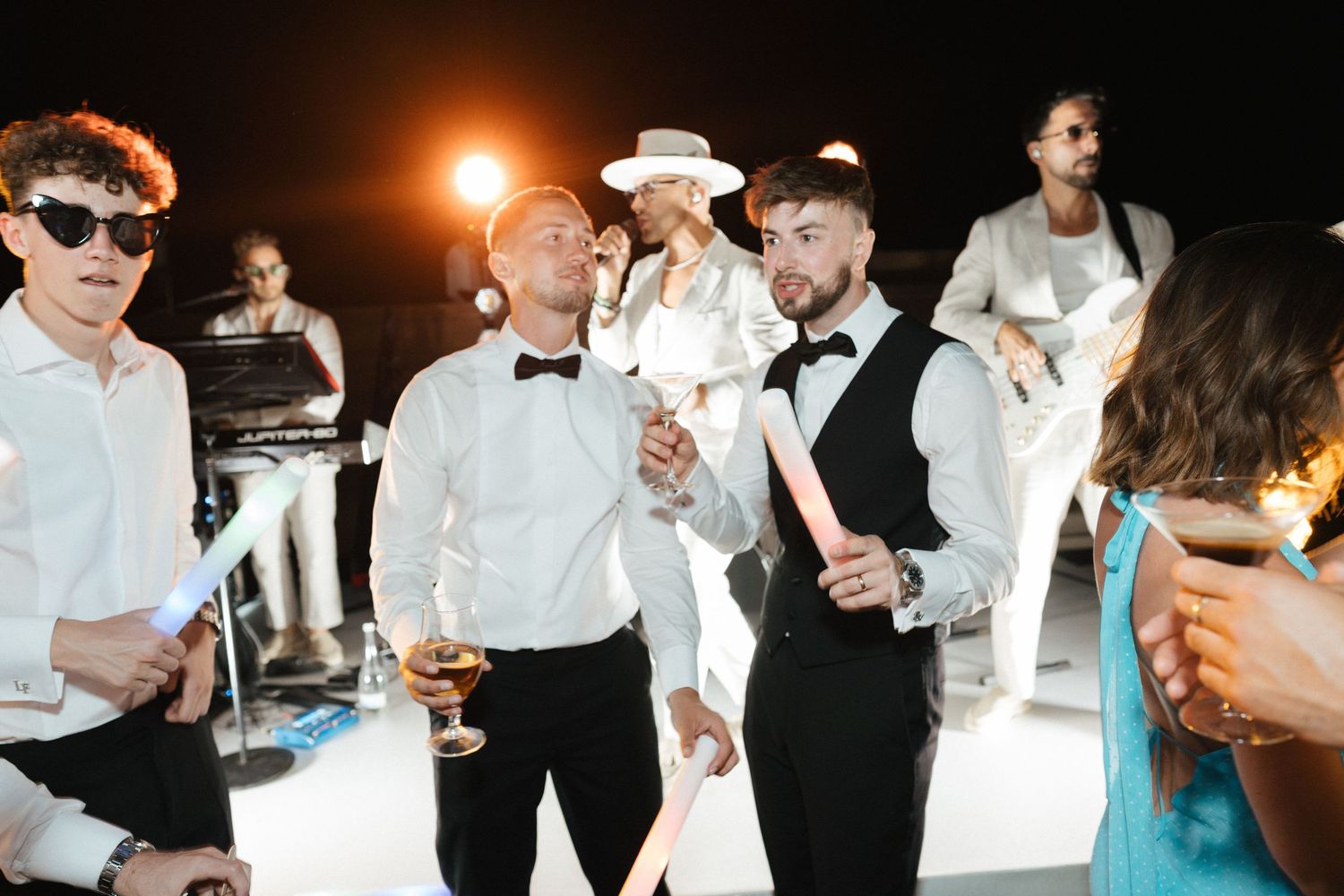 Wedding party guests dancing and celebrating at a reception under warm lighting.