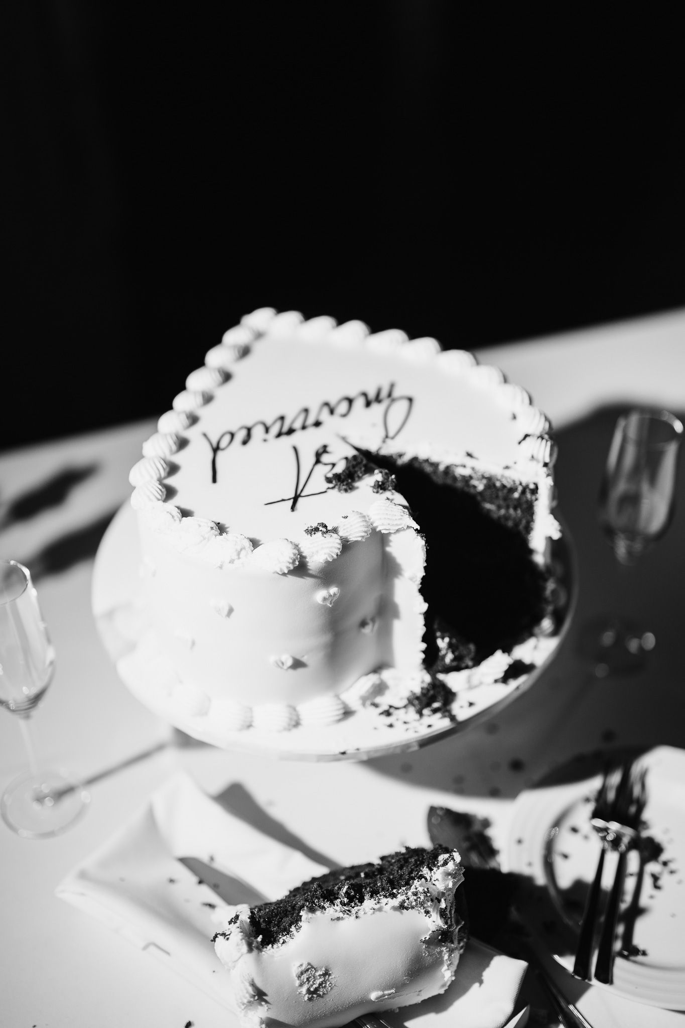 Close-up black and white photo of partially eaten white wedding cake.