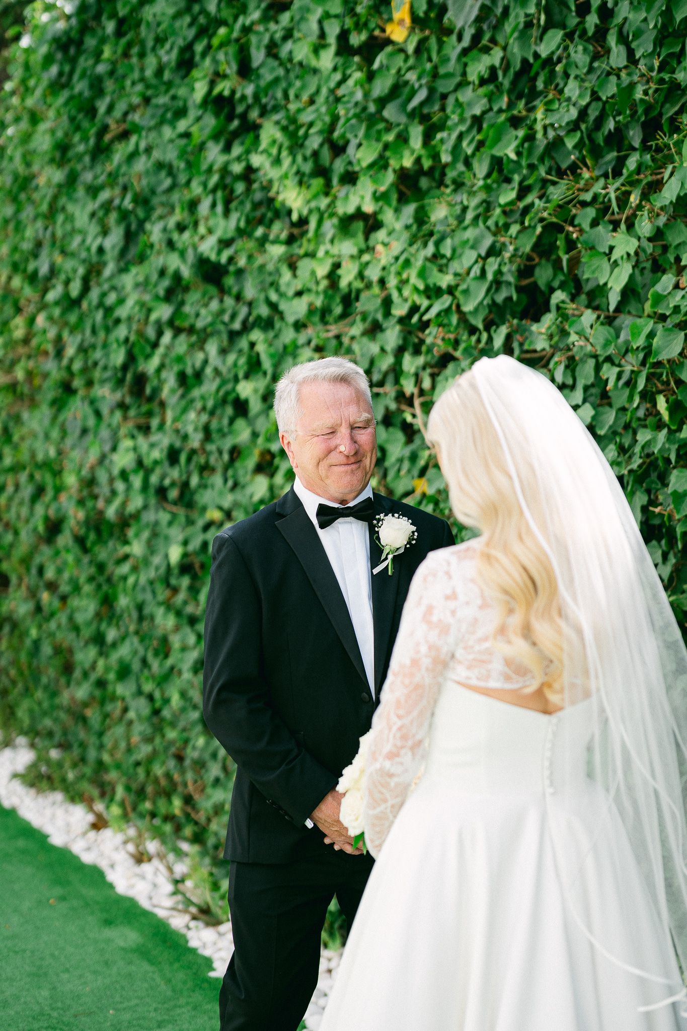 A beautiful first look sequence between a bride and escort against a green garden wall.