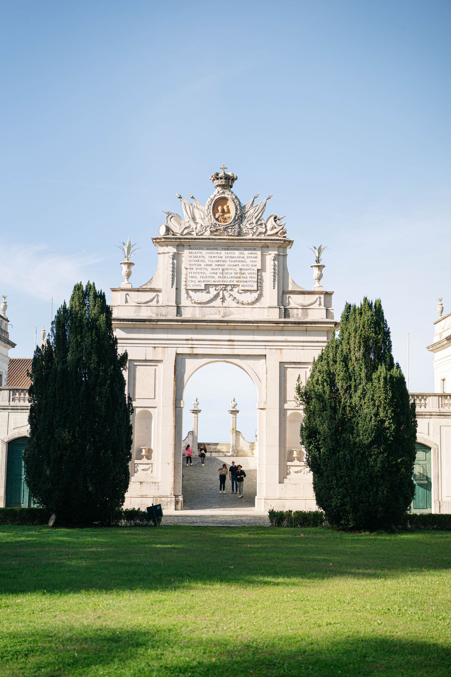 Classical white stone archways and cypress trees frame a majestic garden entrance.