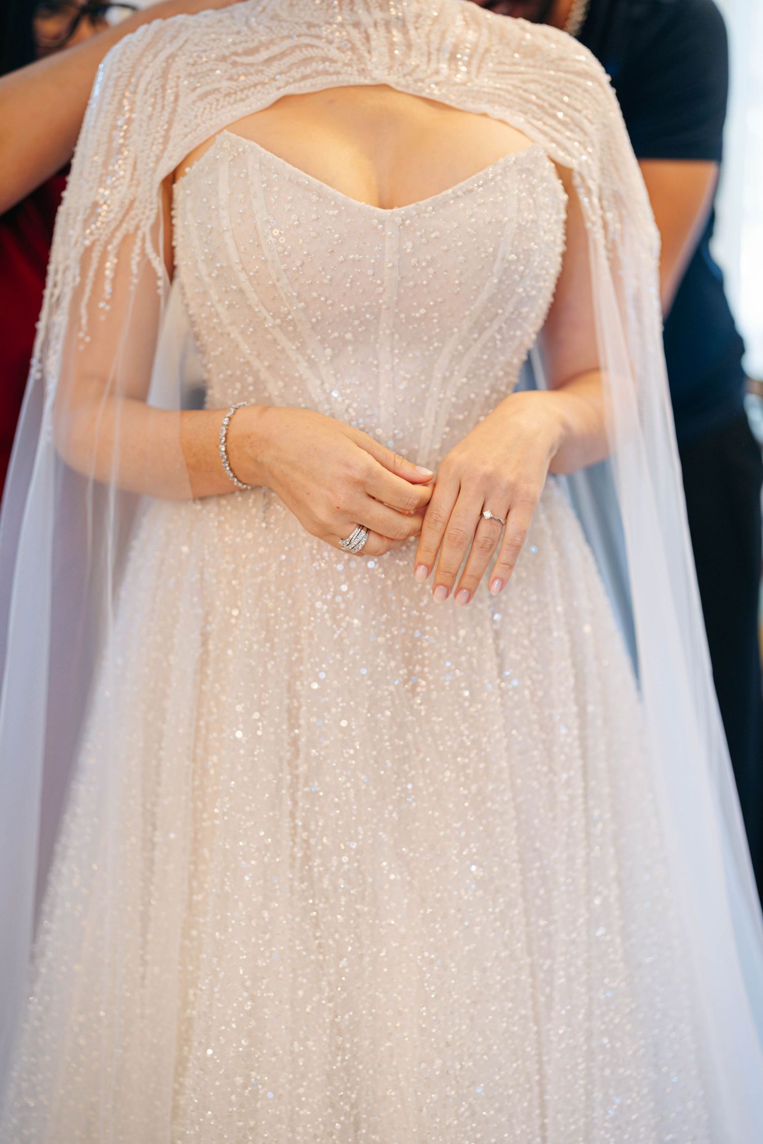 Close-up details of a sparkly white wedding dress with delicate beading and flowing cape sleeves.
