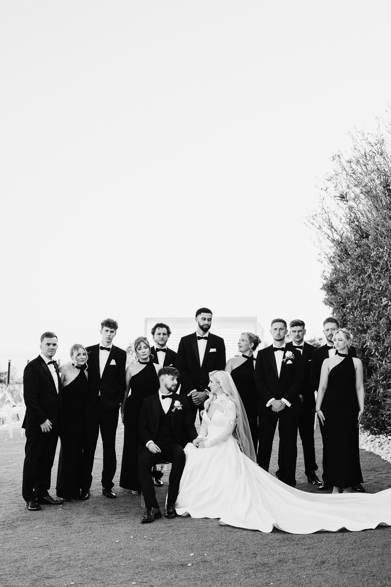 Large wedding party poses for formal group photo outdoors in black and white attire.