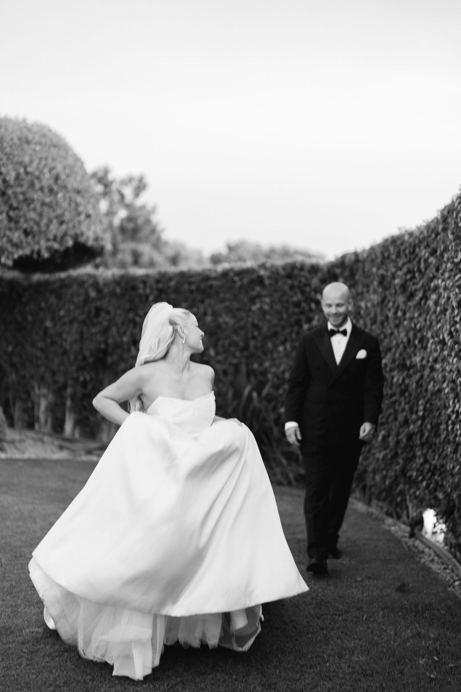 Black and white portrait of bride's flowing dress movement in garden setting.