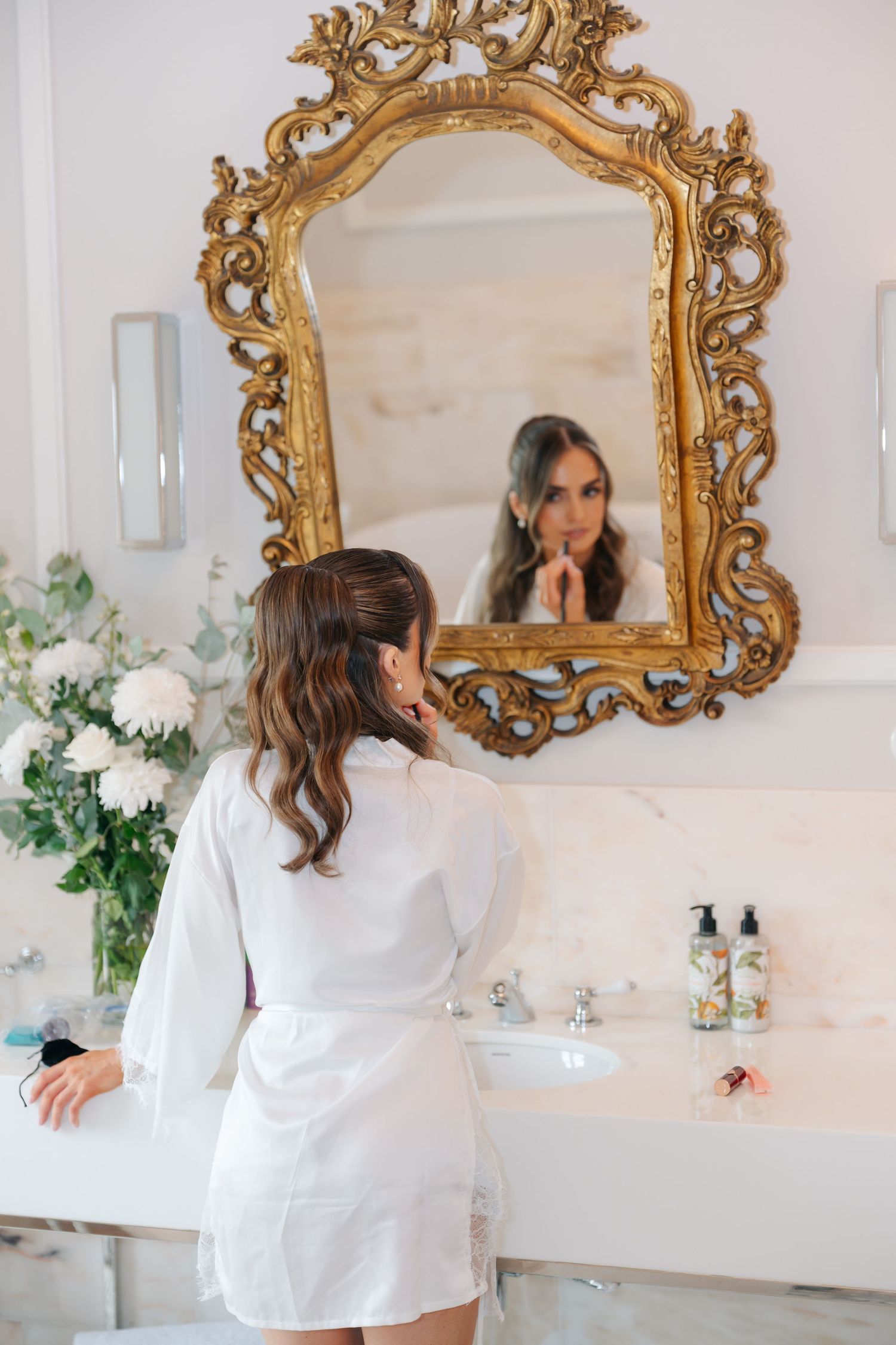 Ornate gold mirror above white bathroom vanity with floral decorations.