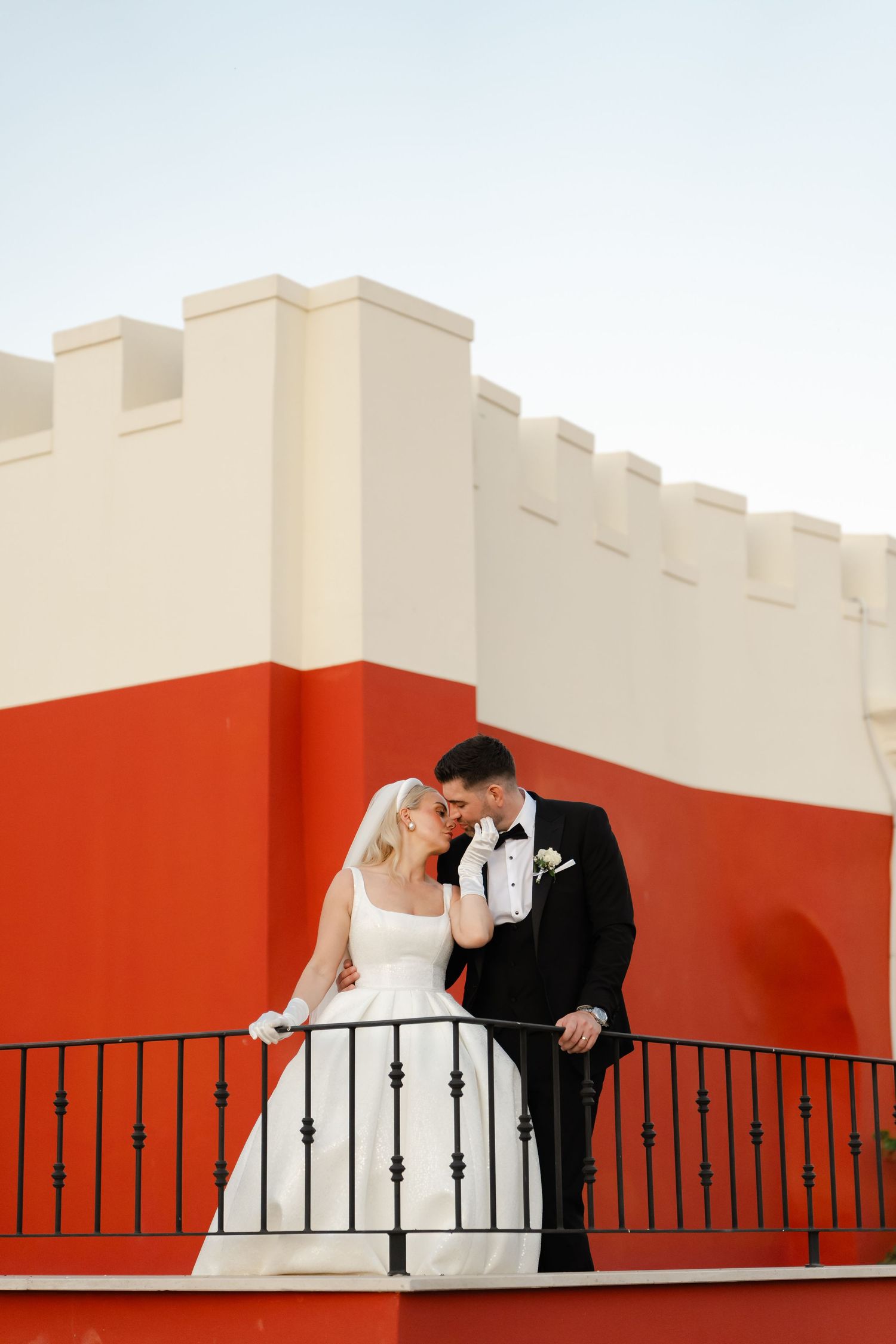 Wedding couple poses romantically against red and white geometric architecture.