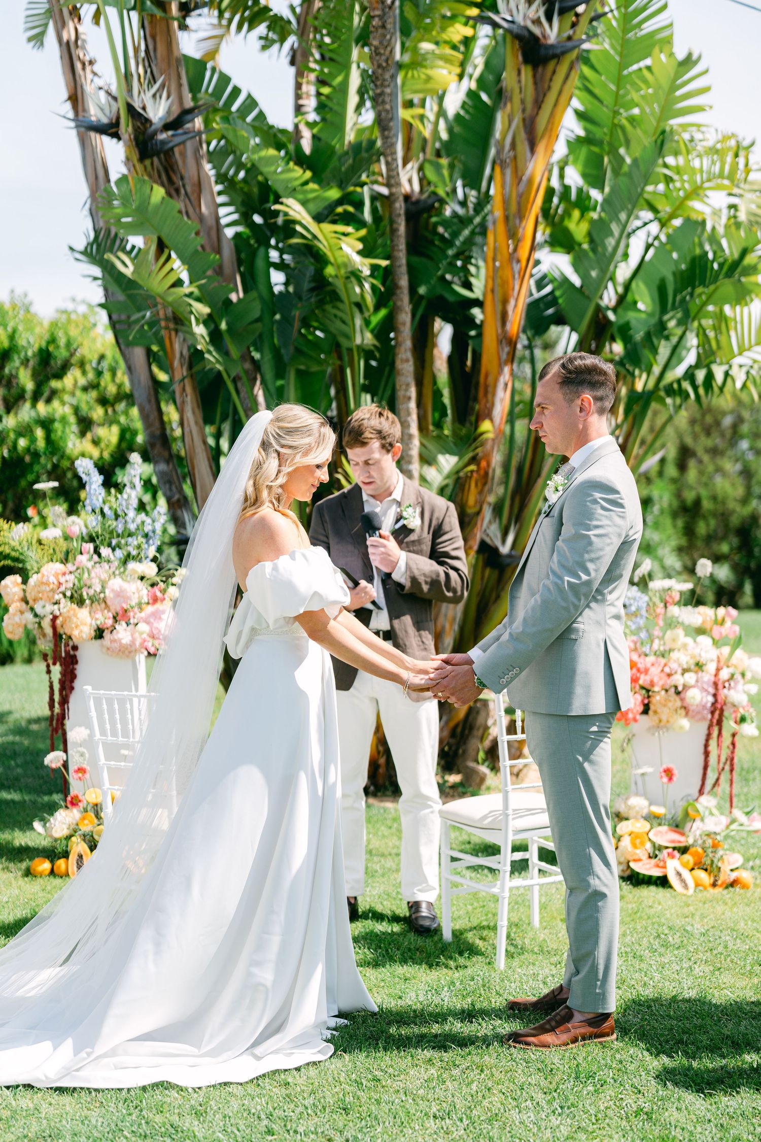Outdoor wedding ceremony with tropical palm trees and white chairs set up on a lush green lawn.