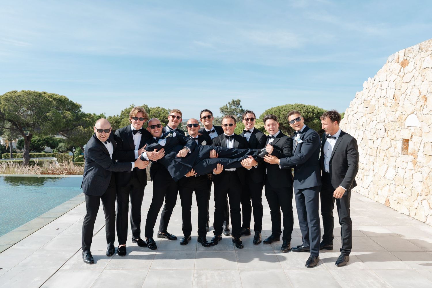 Groomsmen in dark suits posing together at waterfront wedding venue.
