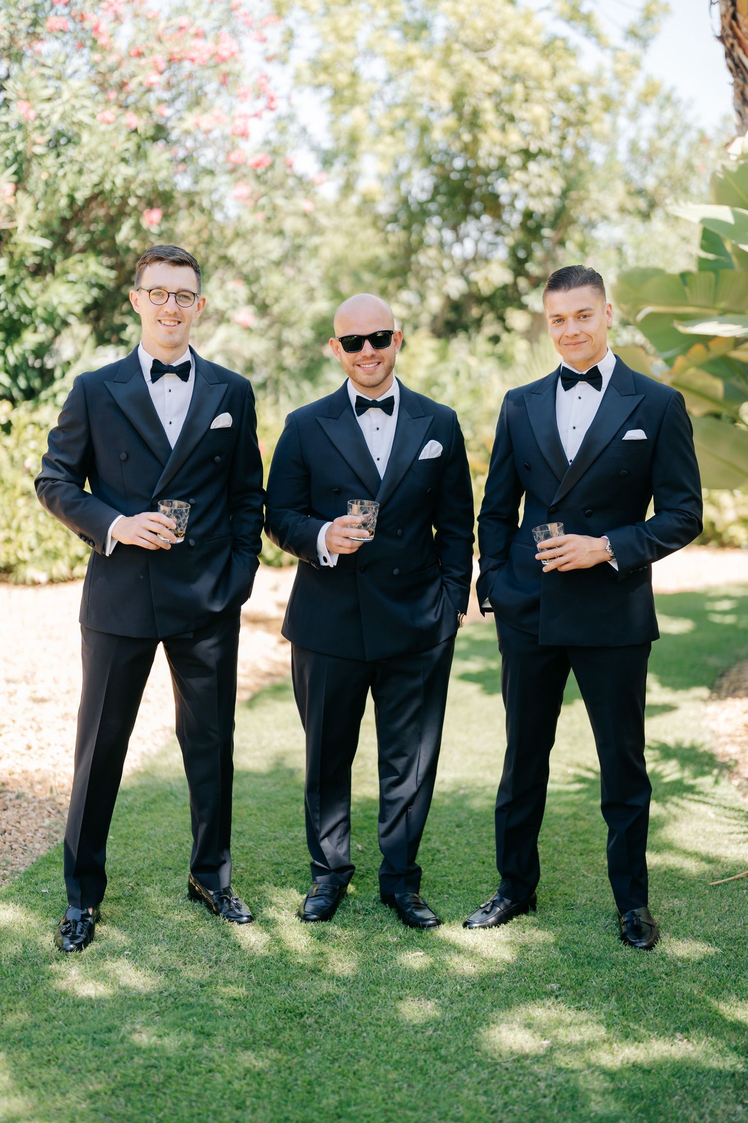 Groomsmen in black tuxedos posing playfully on grass.