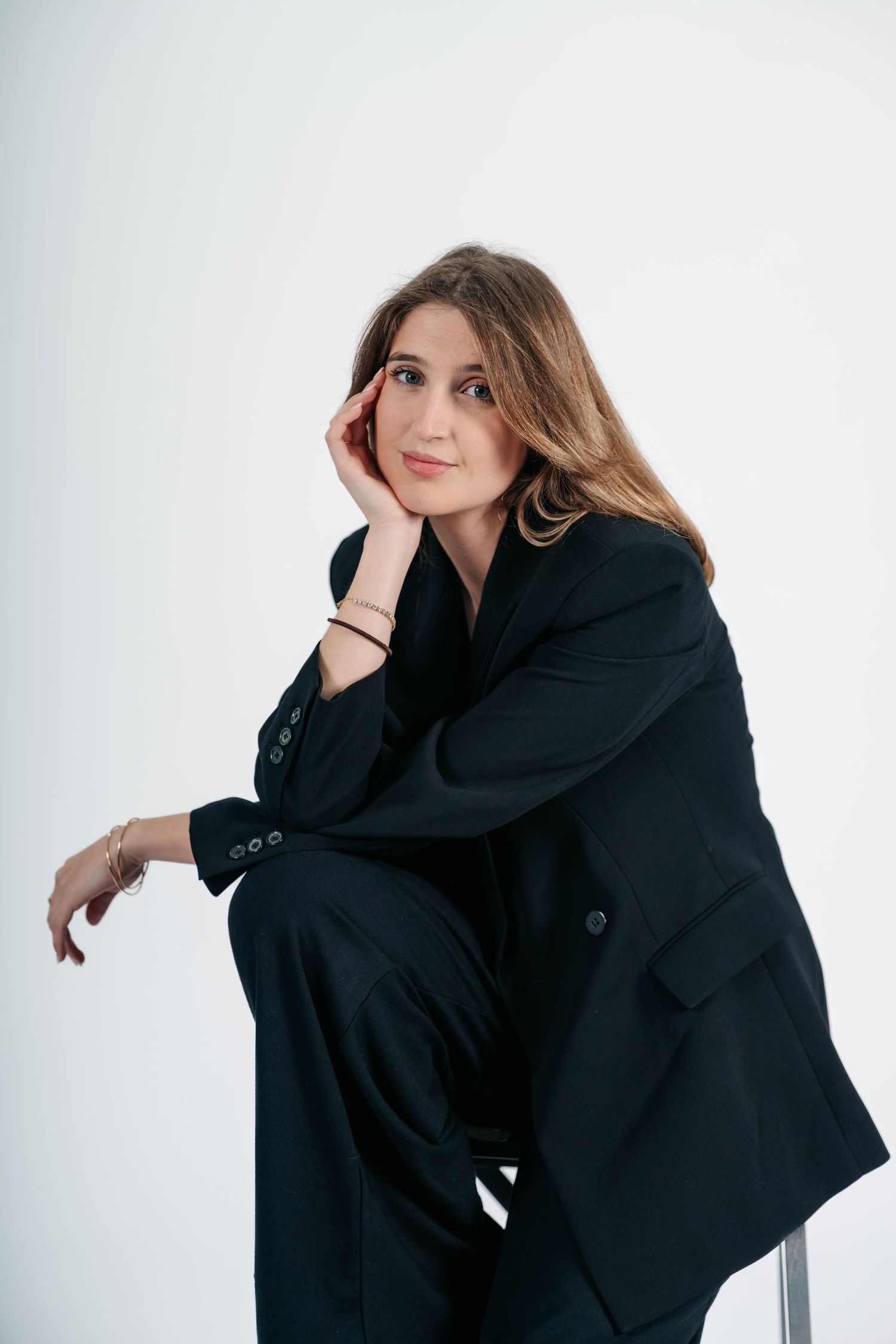 Person in an oversized black blazer poses expressively against a white background in a fashion photoshoot series.