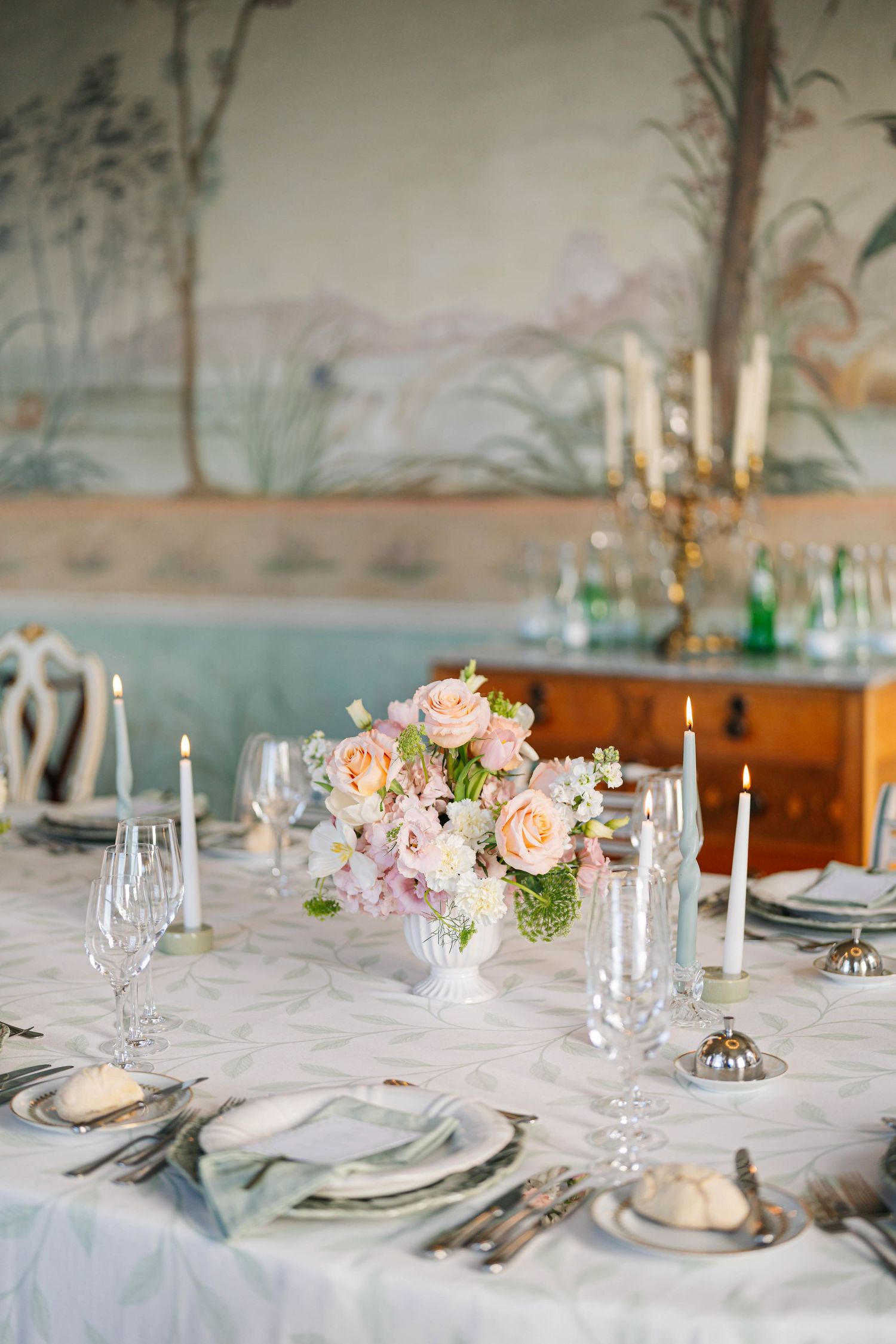 Elegant wedding reception tables with white linens, pink floral centerpieces, taper candles and delicate place settings.