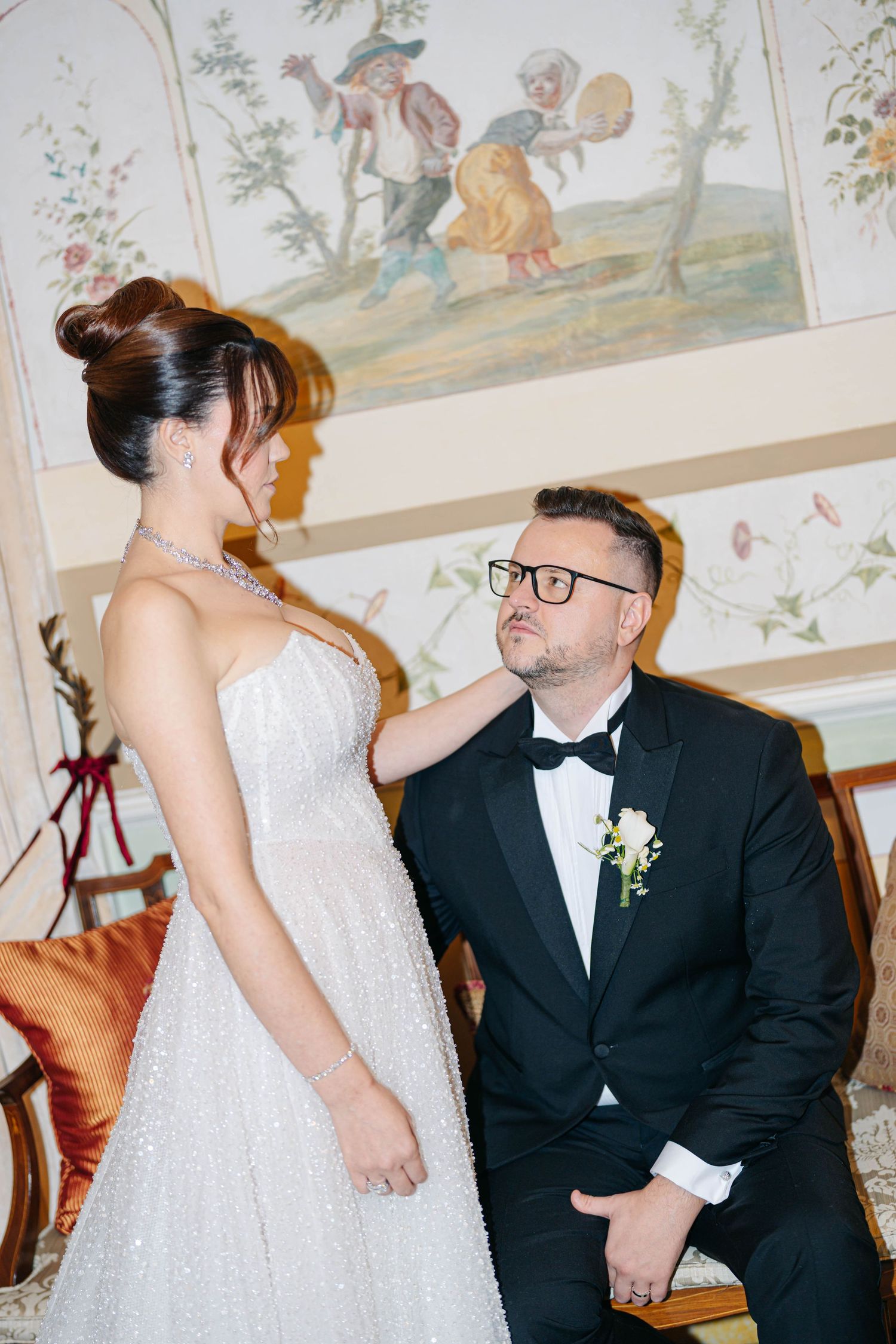 A romantic wedding moment captured indoors with a decorative mural visible on the ceiling.