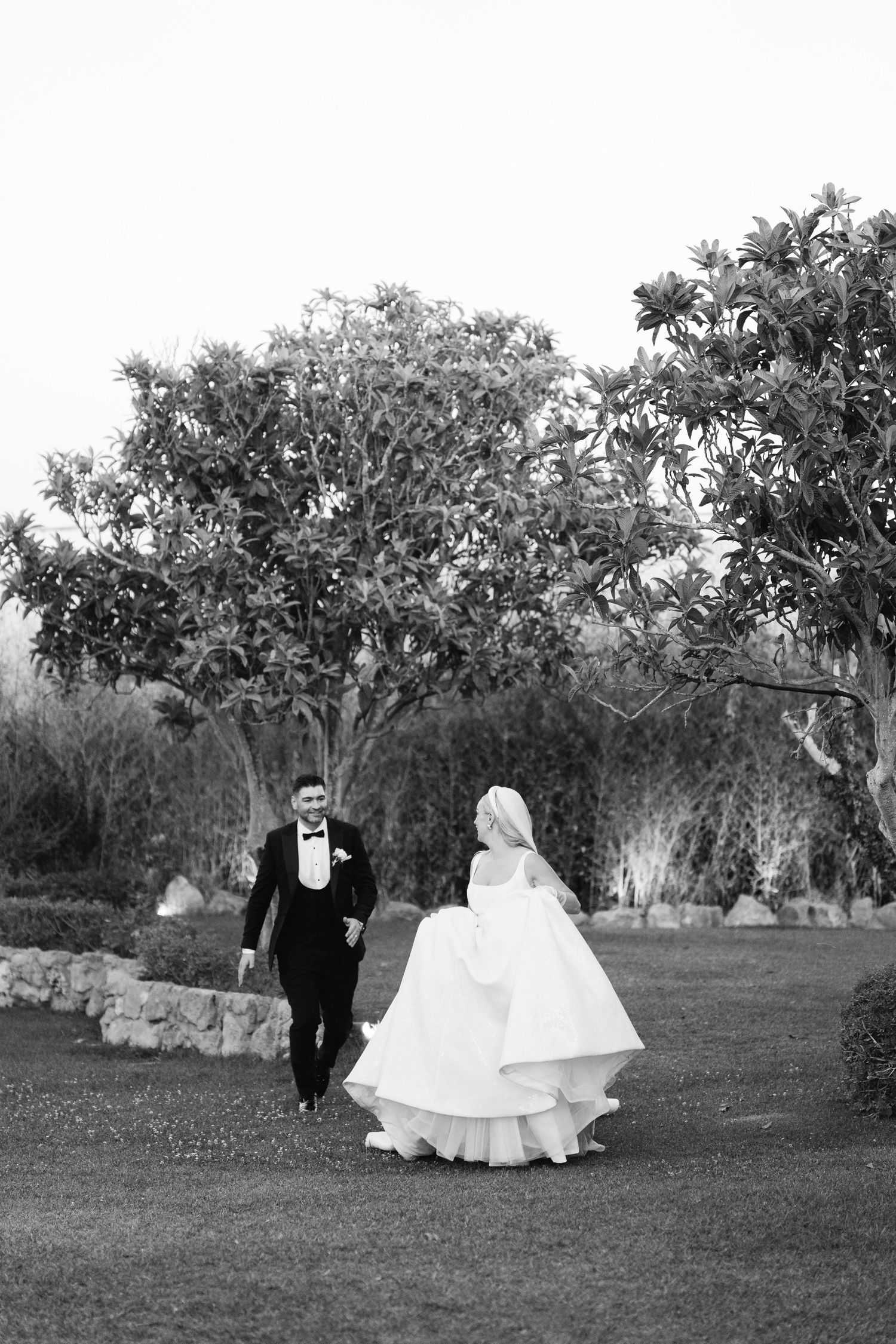 A wedding couple strolls through an outdoor garden setting with natural landscaping.