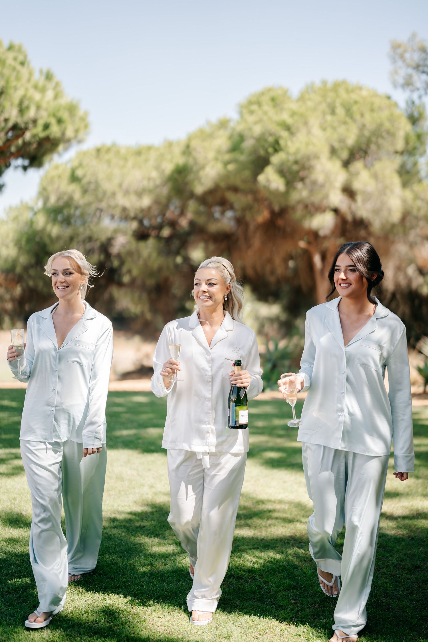 Friends in coordinated white outfits share drinks and laughter in a sunny garden.
