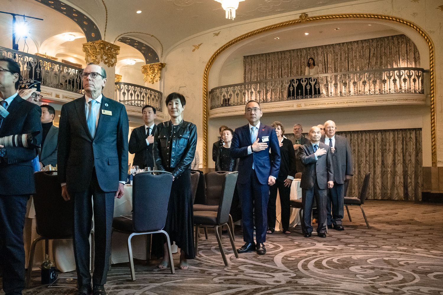 Elegantly dressed guests mingling in a grand ballroom with ornate architecture during a formal event.