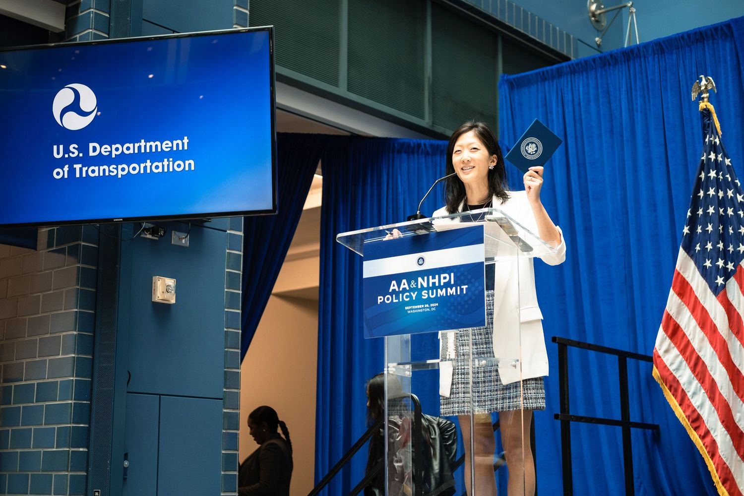 Woman speaking at podium during AANHPI Policy Summit at U.S. Department of Transportation event.