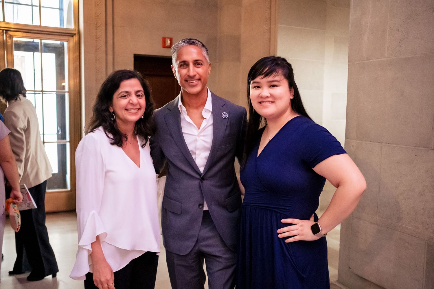 Three professionals smile together in a elegant marble hallway at a formal event.