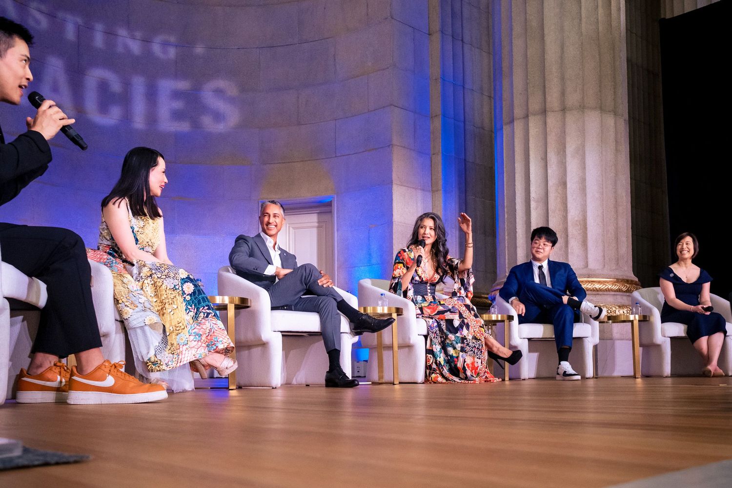 Panel discussion on stage with seven diverse speakers seated in front of a backdrop reading Lasting Legacies.