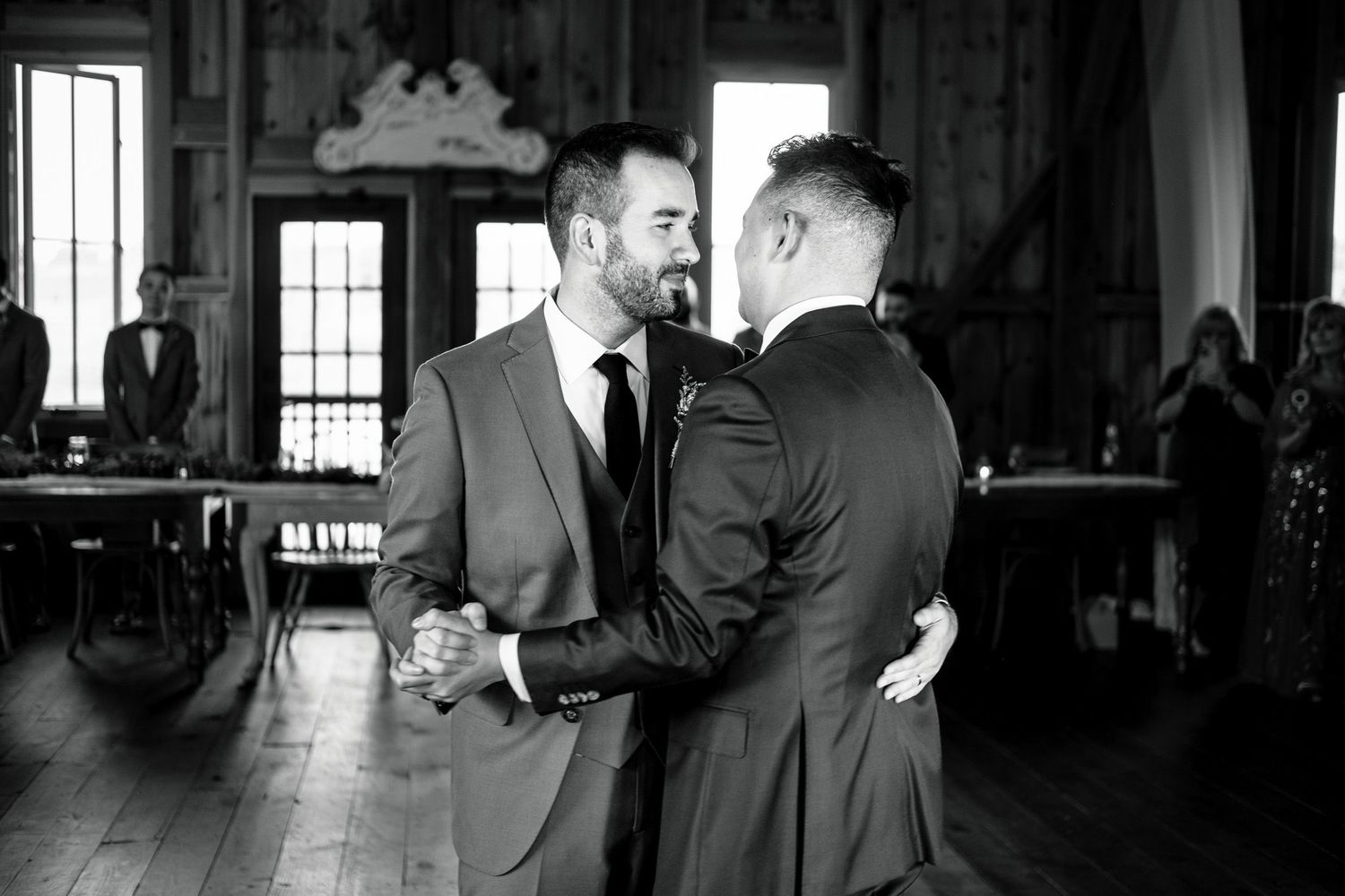 Two grooms share intimate first dance moment in black and white wedding photo.
