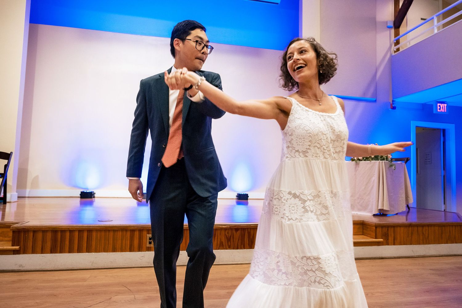 Smiling bride in white dress twirls with groom in dark suit during elegant first dance.