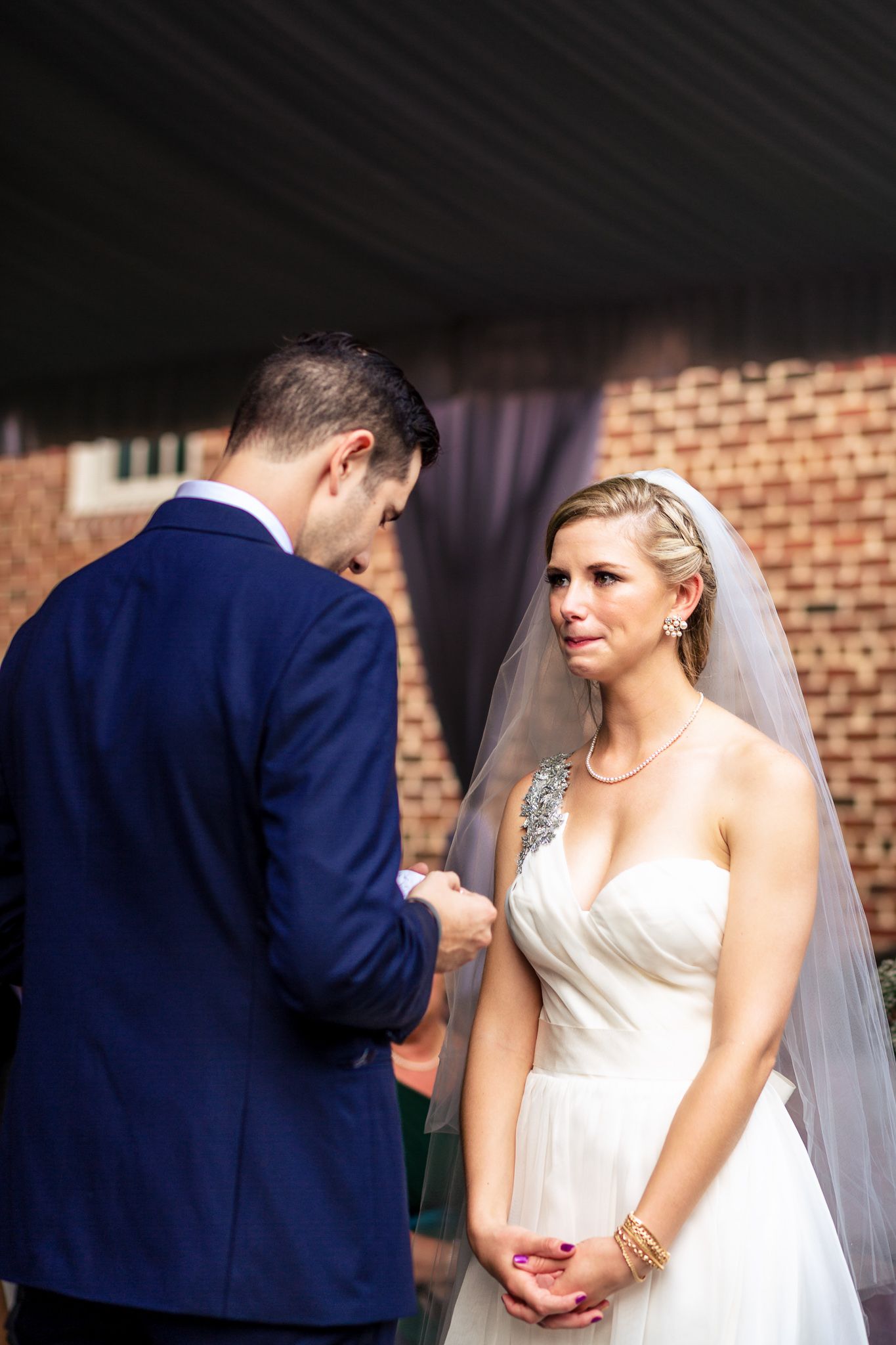 Groom in navy suit exchanges vows with emotional bride in white wedding dress.
