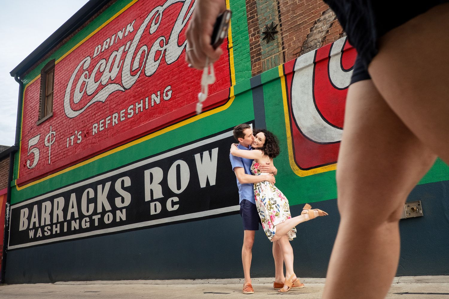 Couple embraces kissing near Barracks Row Coca-Cola mural in Washington DC.
