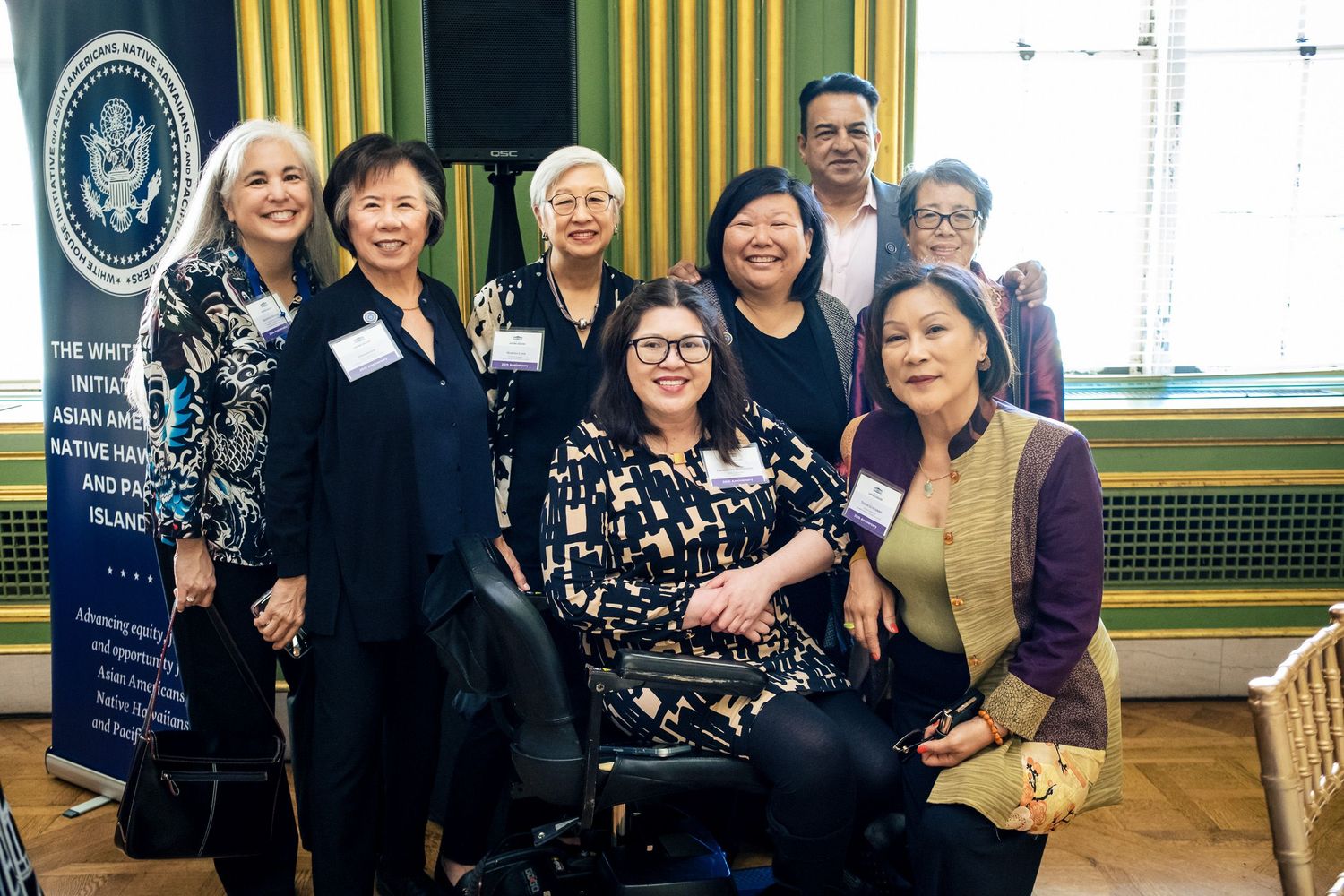 Group of diverse women posing together at a White House AANHPI initiative event, including a woman in a wheelchair.
