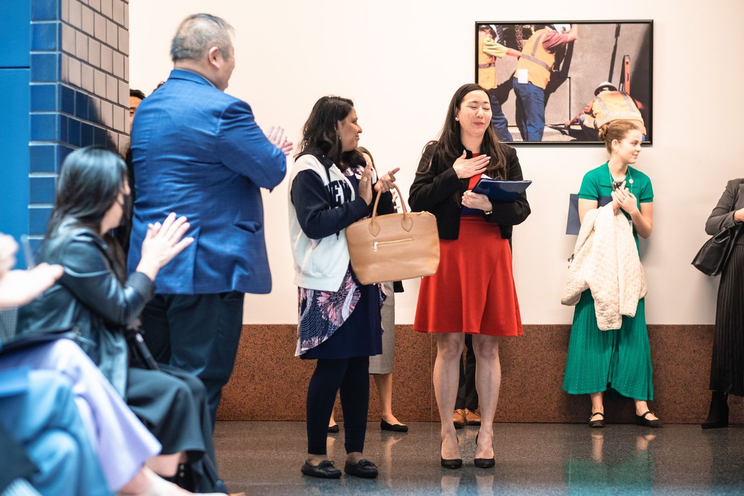 People networking at an art gallery event, with a woman in a red skirt holding a tote bag in the foreground.