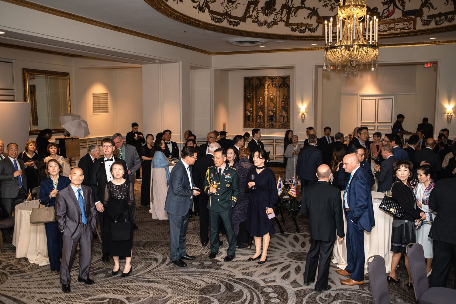 Elegantly dressed guests mingle at a formal military gala event in a grand ballroom.