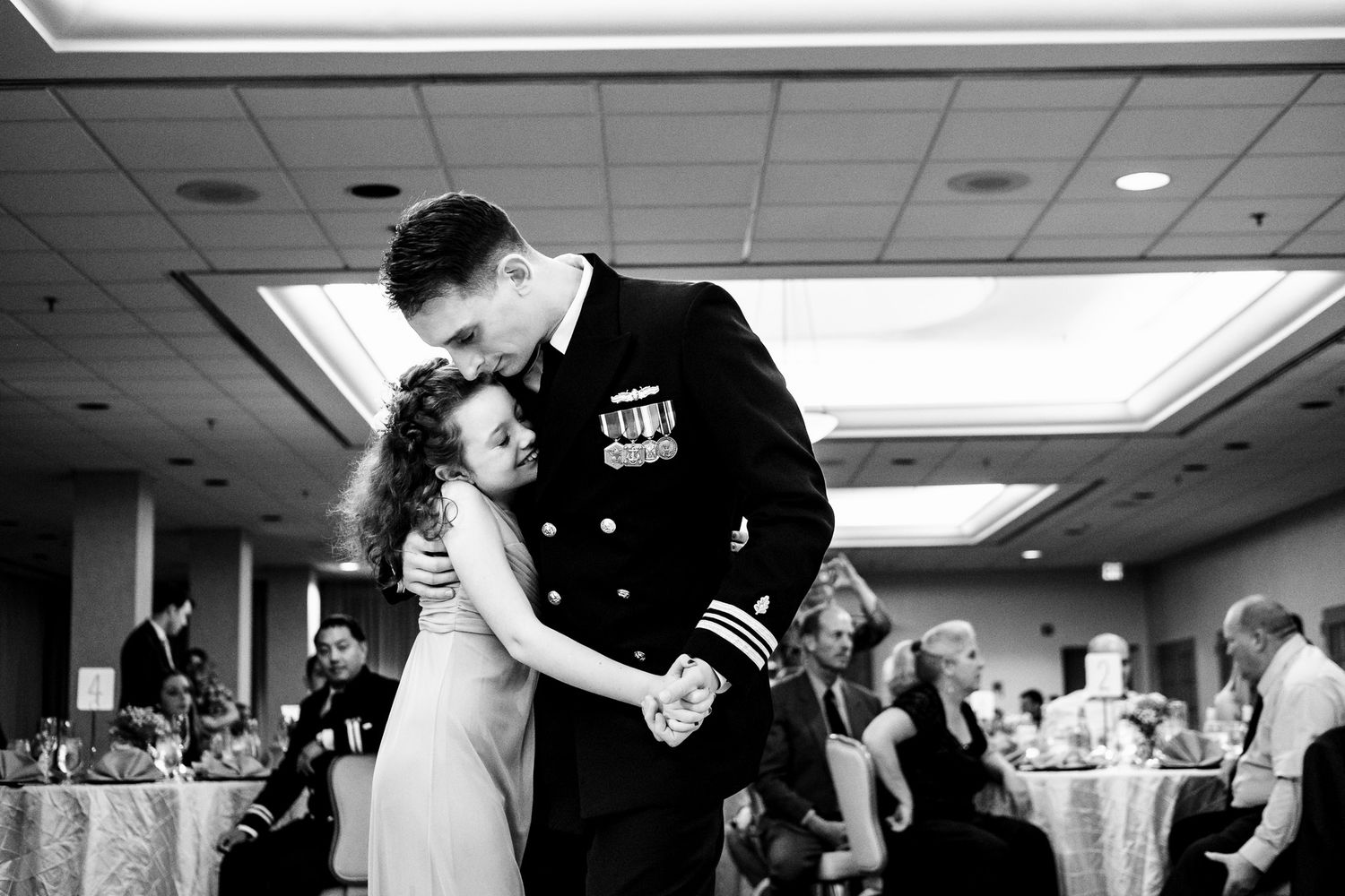 Military groom in dress uniform shares tender first dance with bride at elegant wedding reception.