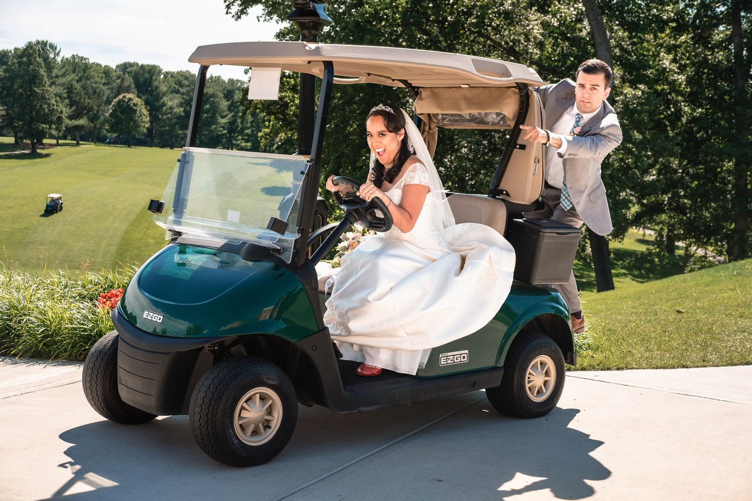 Bride and groom riding a green golf cart on a sunny golf course on their wedding day.