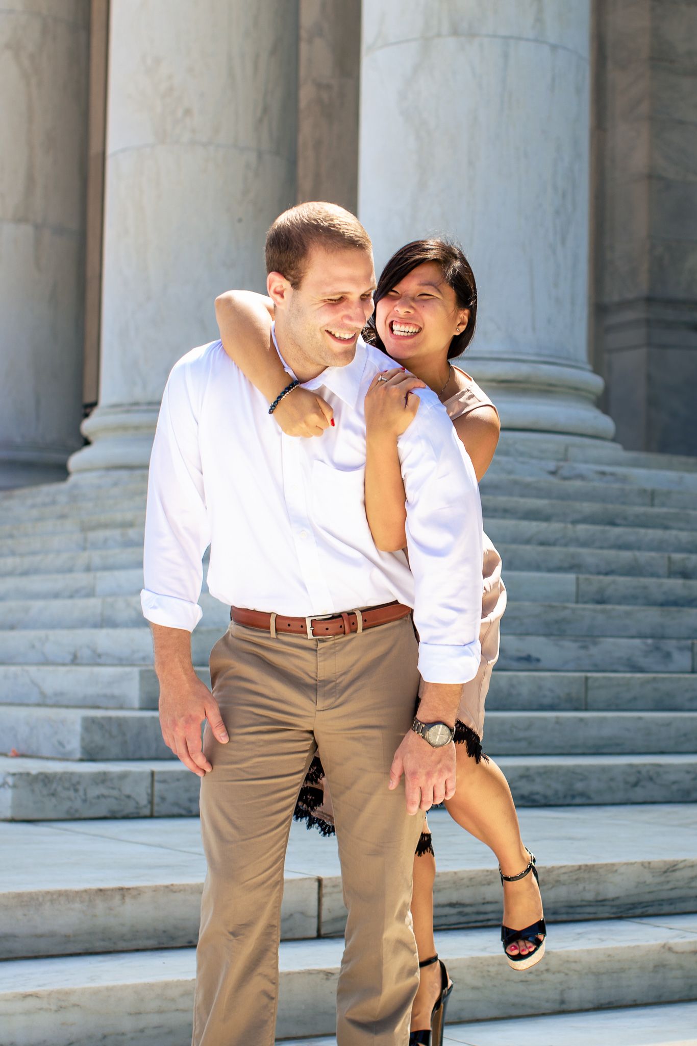 Happy couple laughing together on marble steps with tall columns in an elegant outdoor setting.