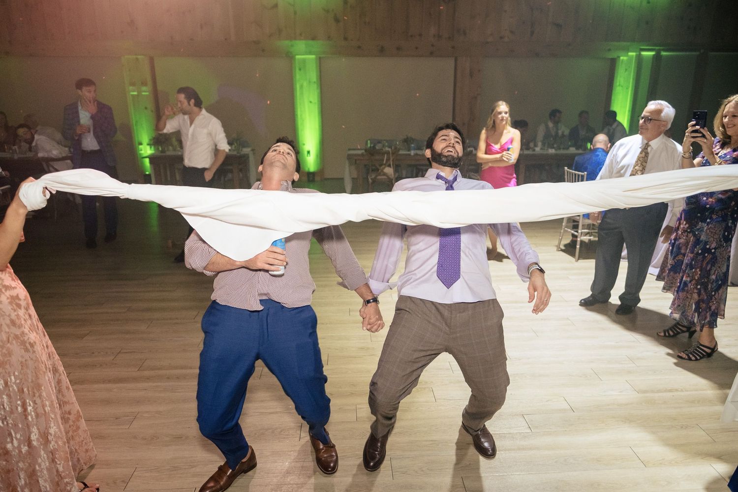 Two wedding guests doing limbo under a white fabric streamer on the dance floor at reception.