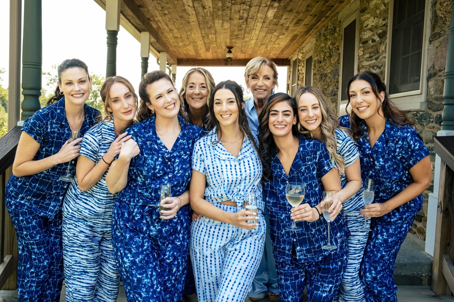 Bridal party in matching blue floral pajamas smiling together on a porch before the wedding.