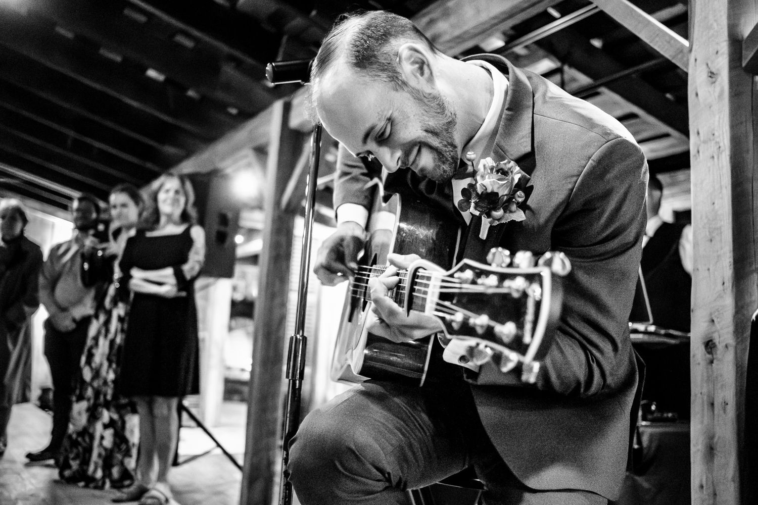 Black and white photo of a guitarist performing passionately at a rustic wedding reception.