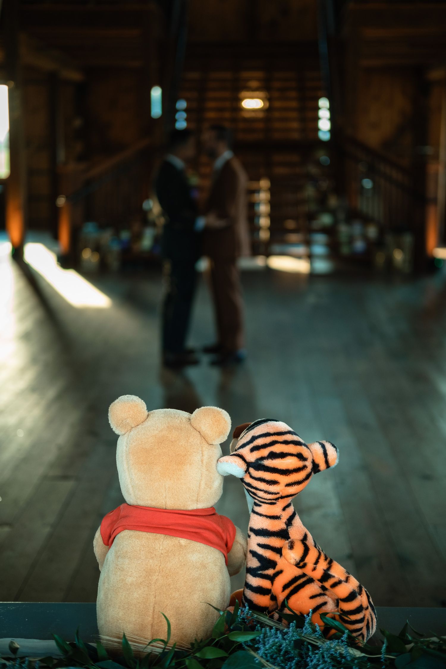 Winnie the Pooh and Tigger plush toys watch two grooms dance at wedding.