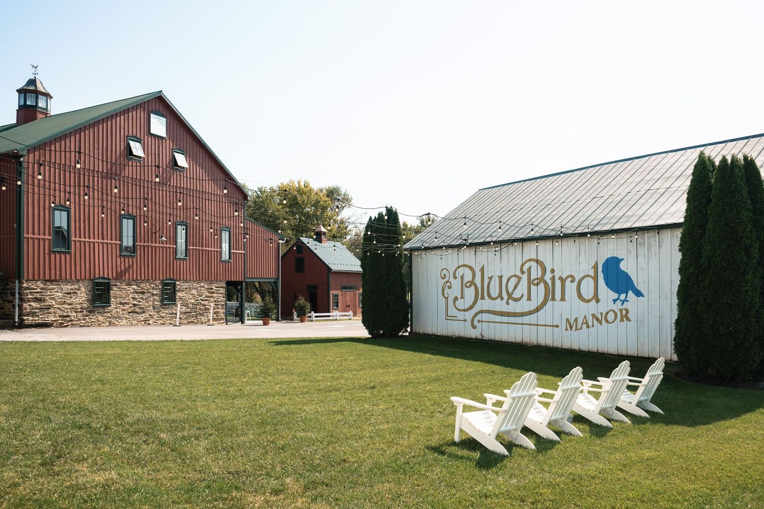 Exterior view of BlueBird Manor wedding venue featuring a red barn and white Adirondack chairs.