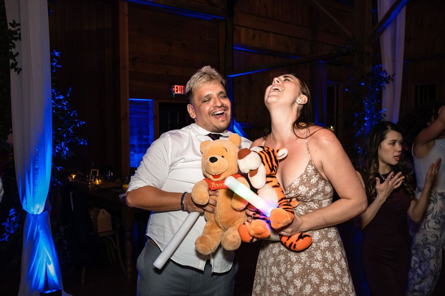 Wedding guests laugh and dance while holding Winnie the Pooh and Tigger stuffed animals.