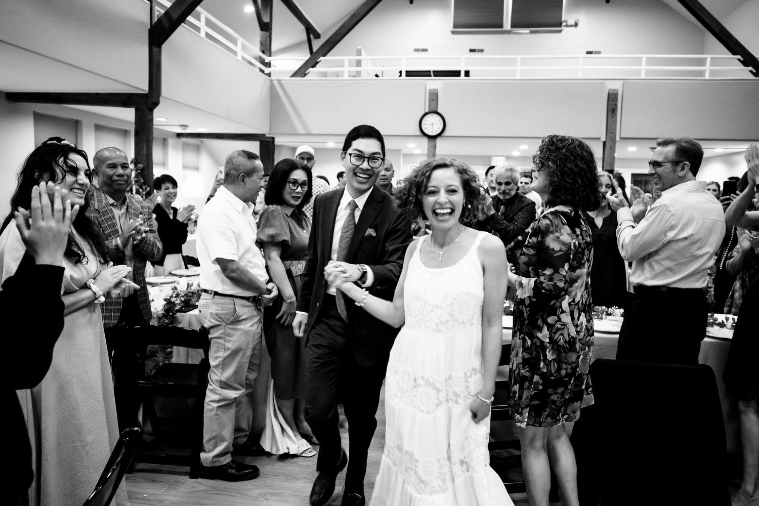 Bride and groom smiling as they enter their wedding reception to applause from guests.