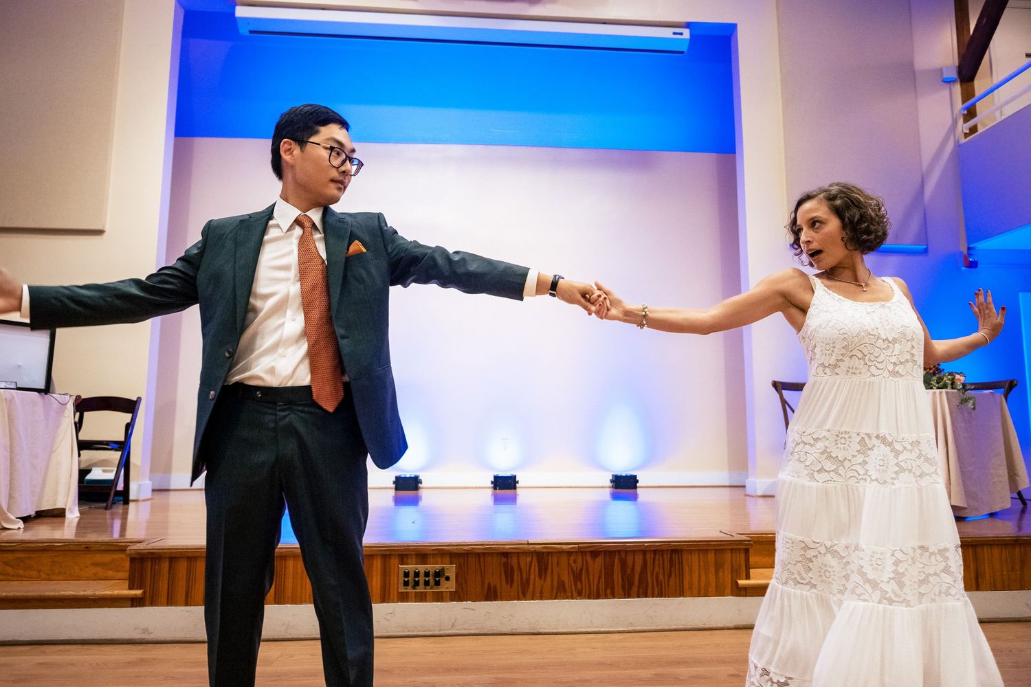 Bride and groom stretch arms wide apart in a dramatic pose during their first wedding dance.
