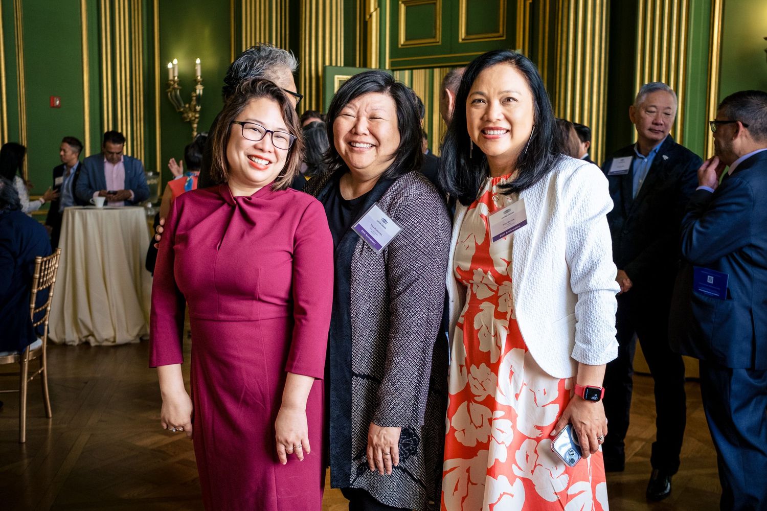 Three women smiling and posing together at an elegant green-walled formal event venue.