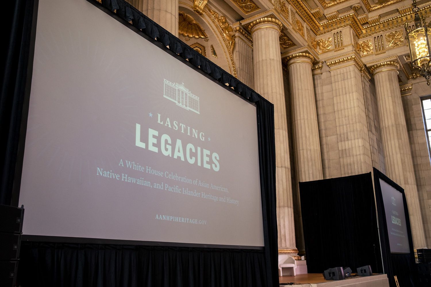 A large projection screen displays 'Lasting Legacies' presentation in a grand hall with ornate columns.