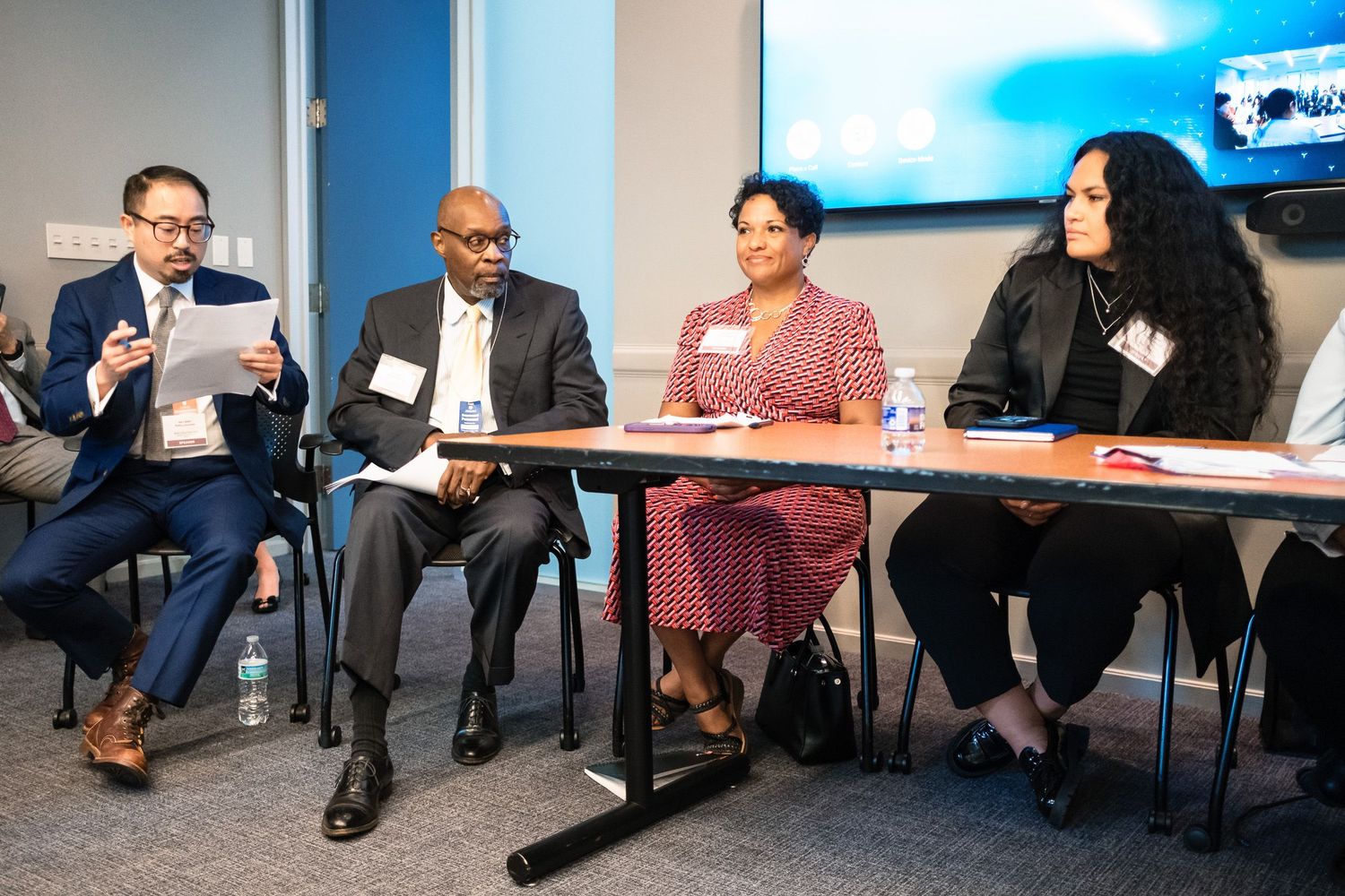 Four professionals sit at a panel discussion table in a conference room, engaged in conversation.