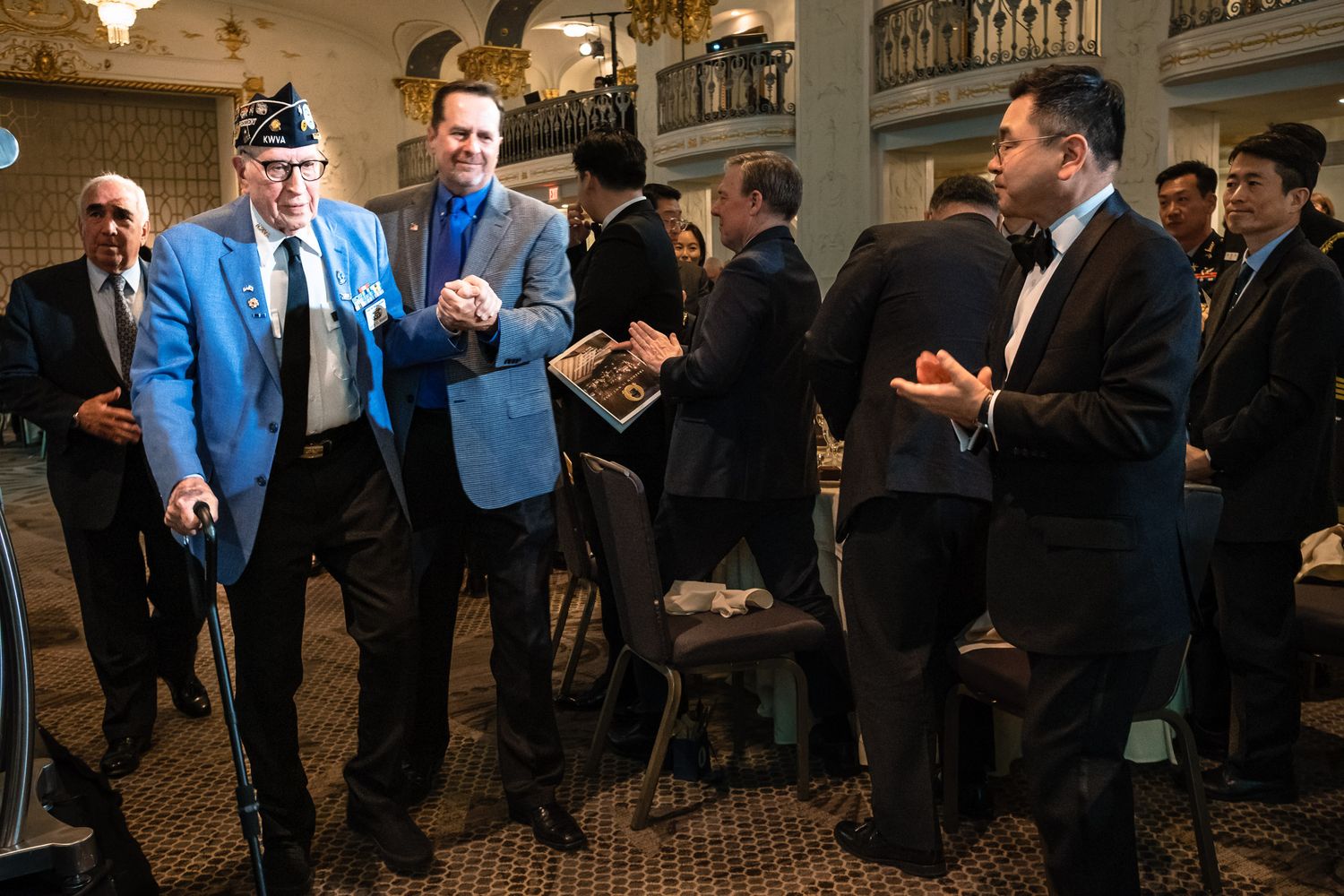Veterans in formal attire socializing and shaking hands at an elegant indoor event or ceremony.
